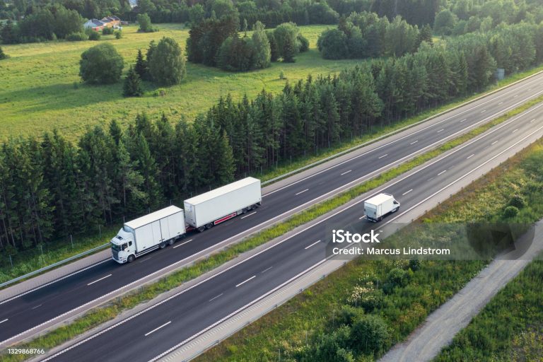 A truck with trailer and a delivery truck travelling in opposite directions on a highway in summer.